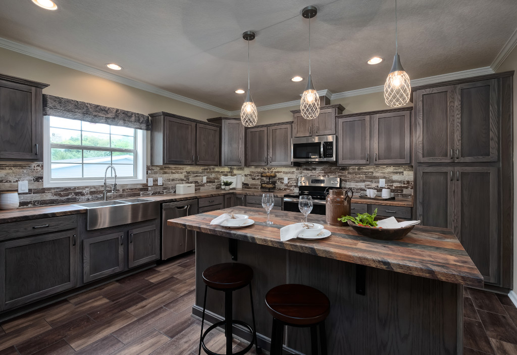 Modern kitchen with dark wood cabinets, a central island with two stools, and three pendant lights. Stainless steel appliances and a window enhance brightness.