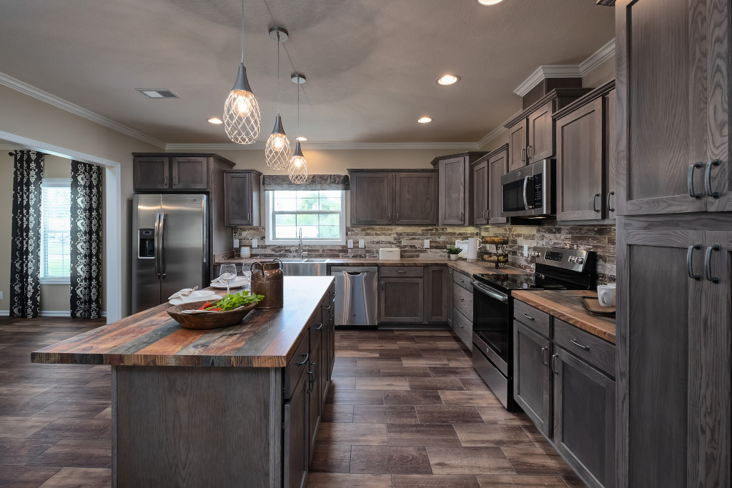 Modern kitchen with rustic charm, featuring gray wooden cabinets, a central island with wooden countertops, pendant lighting, and a stainless steel fridge.