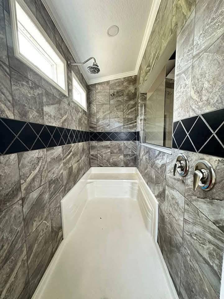 A modern shower with gray marble-patterned tiles and a white tub. Black diamond accent tiles wrap around. Dual controls and a showerhead are visible.