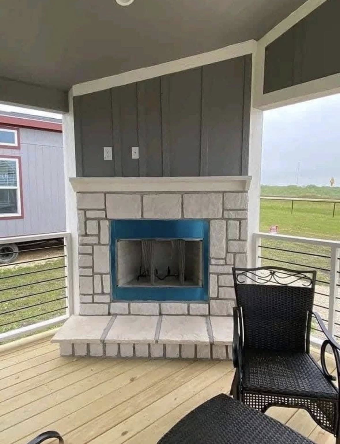 Stylish porch featuring a stone fireplace with a blue accent, surrounded by wicker chairs. The setting overlooks a grassy landscape, exuding a cozy, serene vibe.