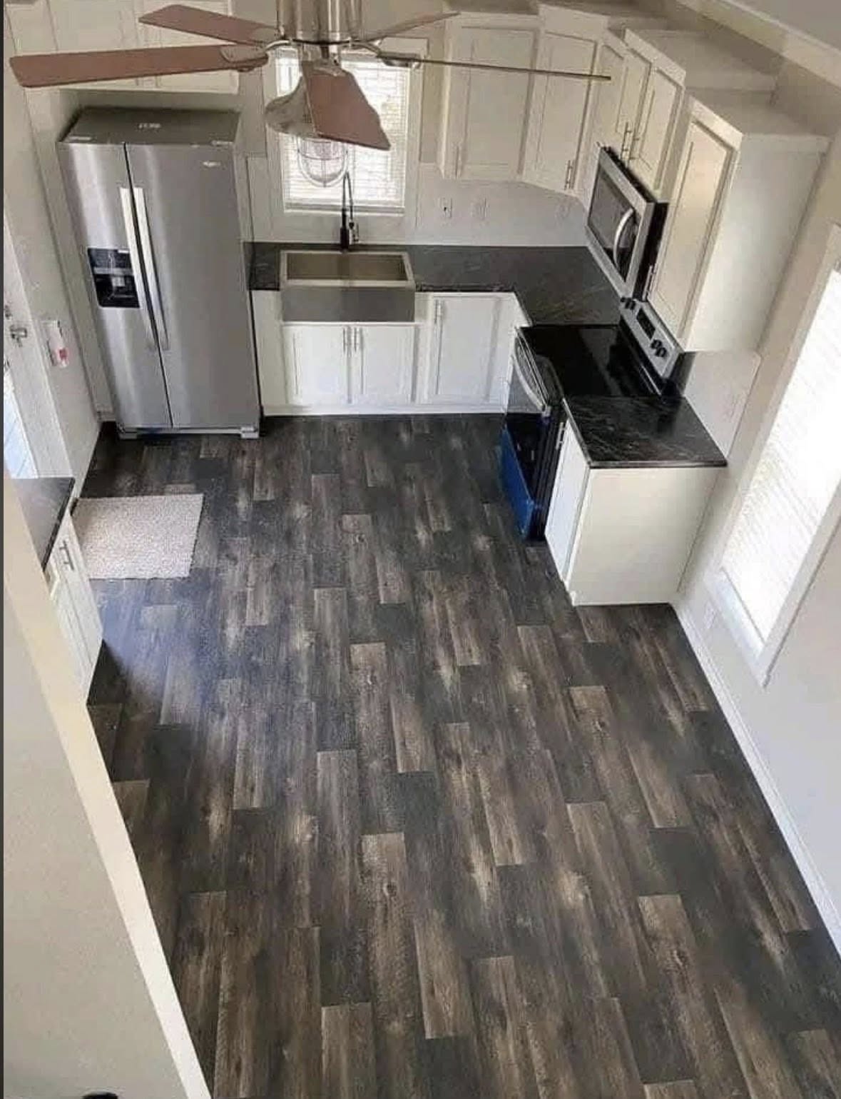 Modern kitchen with dark wood flooring, white cabinets, and stainless steel appliances, including a double-door fridge and built-in microwave.