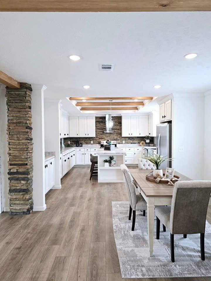 Spacious, modern kitchen with white cabinets, wood beams, and a stone accent wall. Includes a dining table with chairs, creating a cozy, inviting atmosphere.
