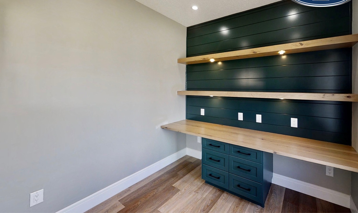 A modern study nook features dark green shiplap walls with wooden shelves and a desk. Warm lighting adds a cozy, inviting ambiance.