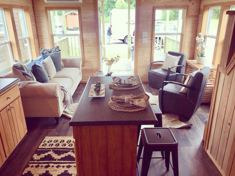 Cozy living area of a tiny home with a beige sofa, two armchairs, and a wood island. Warm, inviting atmosphere with natural light and soft textures.