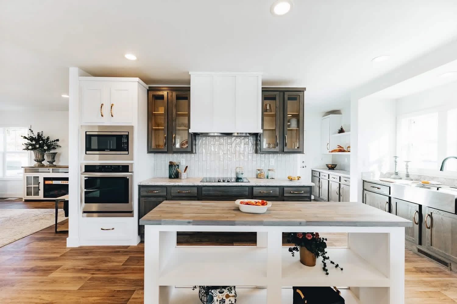 Modern kitchen with white and wooden accents, featuring a central island with a fruit bowl, sleek cabinets, and stainless steel appliances under soft lighting.