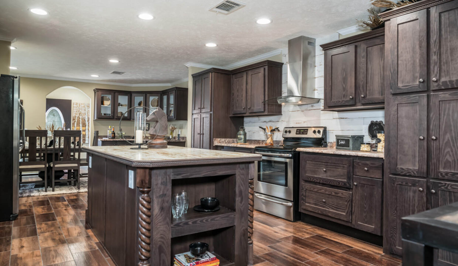 Spacious kitchen with dark wood cabinets and island, stainless steel appliances, and hardwood floors. Dining table visible in the background. Cozy ambiance.