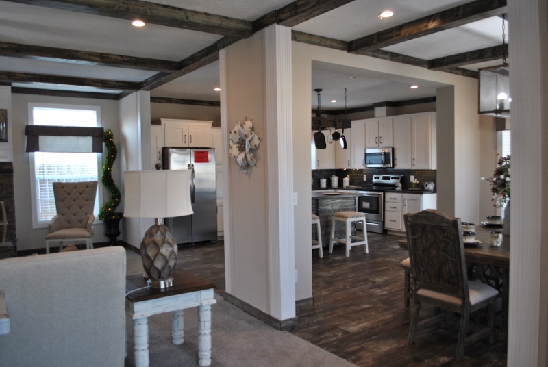 Spacious kitchen and dining area with light walls and dark wood beams. Features modern appliances, elegant furniture, and soft lighting, creating a cozy atmosphere.