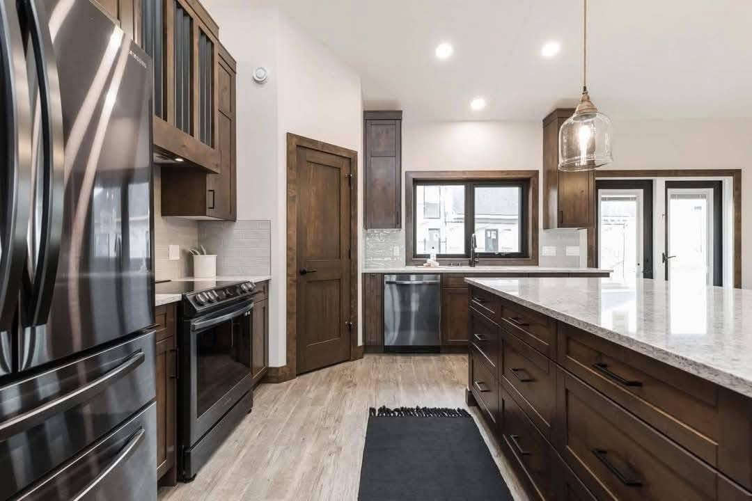 Modern kitchen with dark wood cabinets and light granite countertops. Stainless steel appliances enhance the sleek design. Bright lighting.