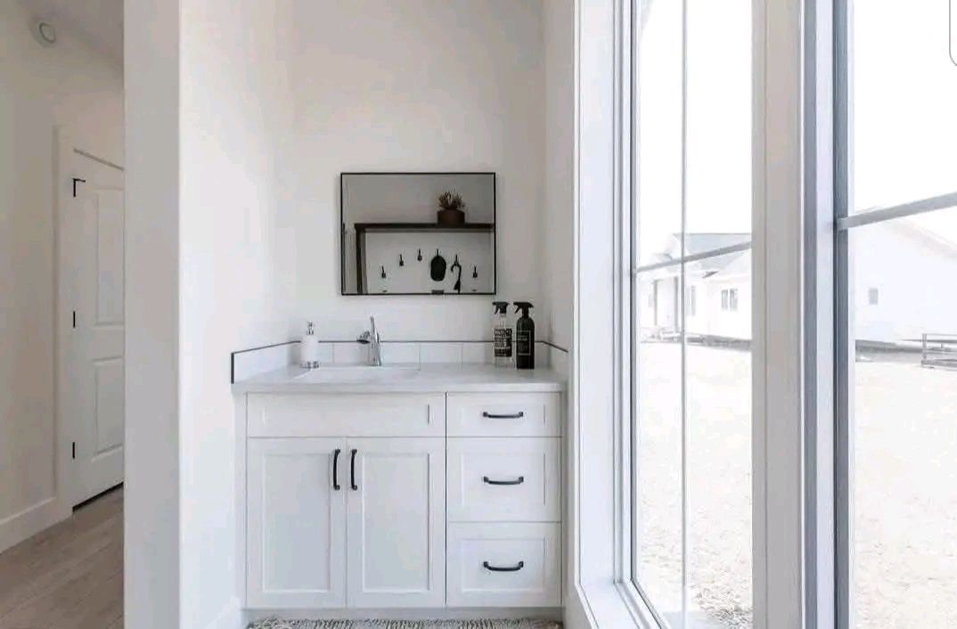 Bright bathroom with a white vanity and black handles, featuring a large mirror and toiletries. Sunlight streams through the window, adding warmth.