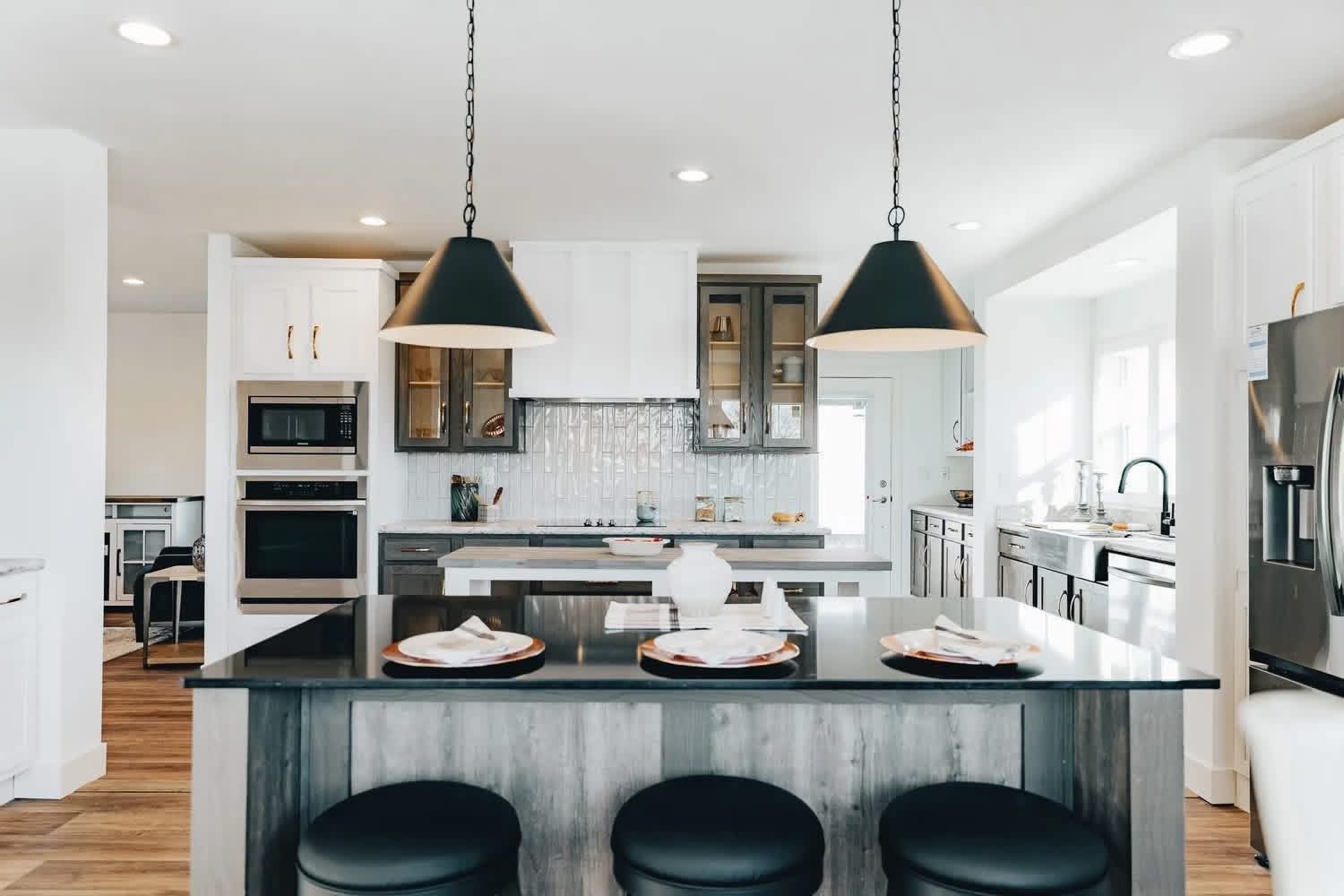 Sleek modern kitchen with a large island, black pendant lights, white cabinets, stainless steel appliances, and wood flooring. Bright and inviting space.