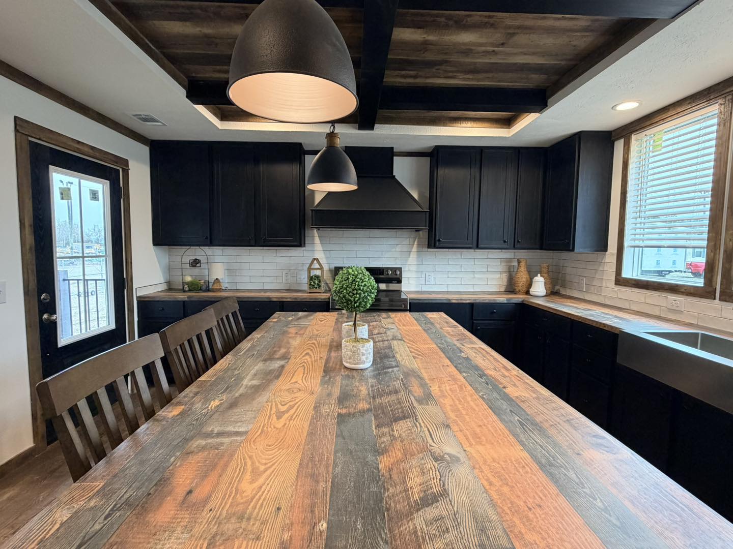 Rustic kitchen with dark cabinets, wooden beams, and a striped wooden island. Black pendant lights hang above, creating a warm, inviting ambiance.