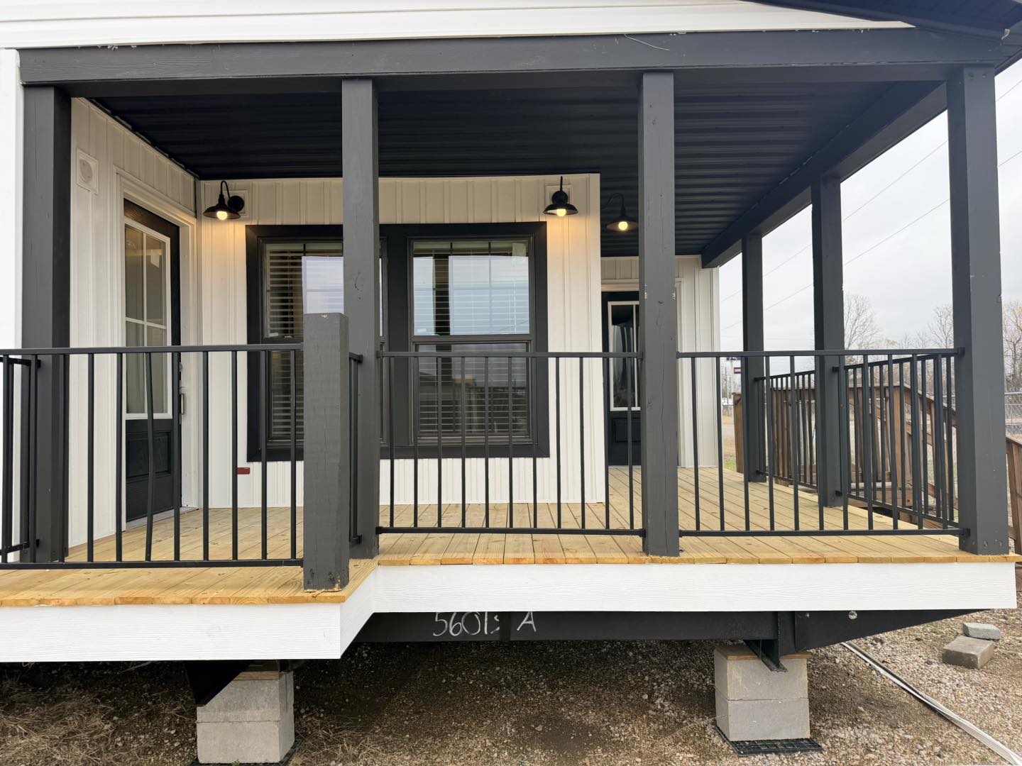 Modern porch with black railings and posts on a wooden deck. White siding, black window frames, and warm lighting create a welcoming feel.