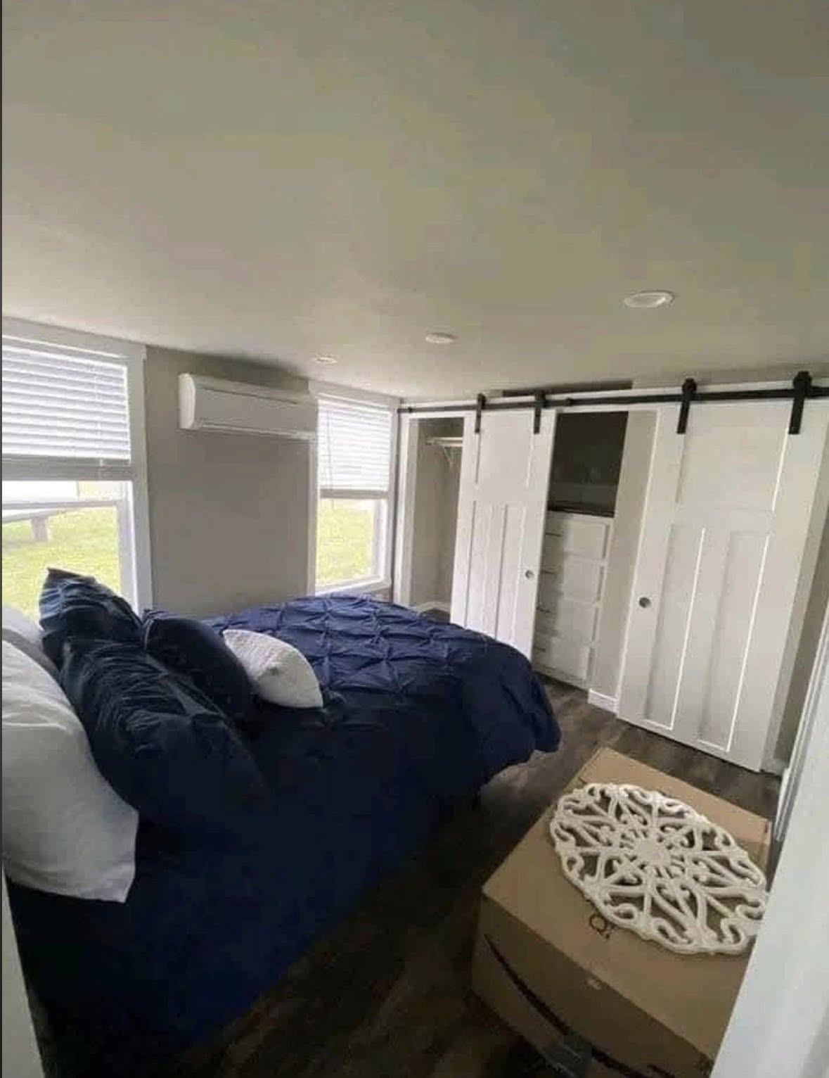 Small bedroom with a blue bed, white pillows, and barn-style sliding closet doors. Sunlight enters through windows, creating a cozy, modern atmosphere.