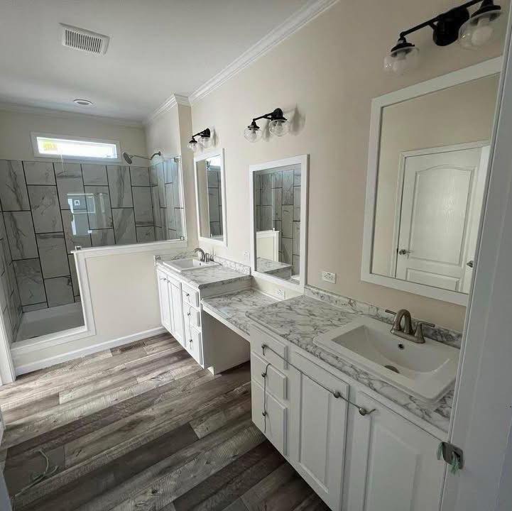 Modern bathroom with dual sinks on marble countertops, white cabinets, a large mirror, industrial light fixtures, and a glass-enclosed shower.