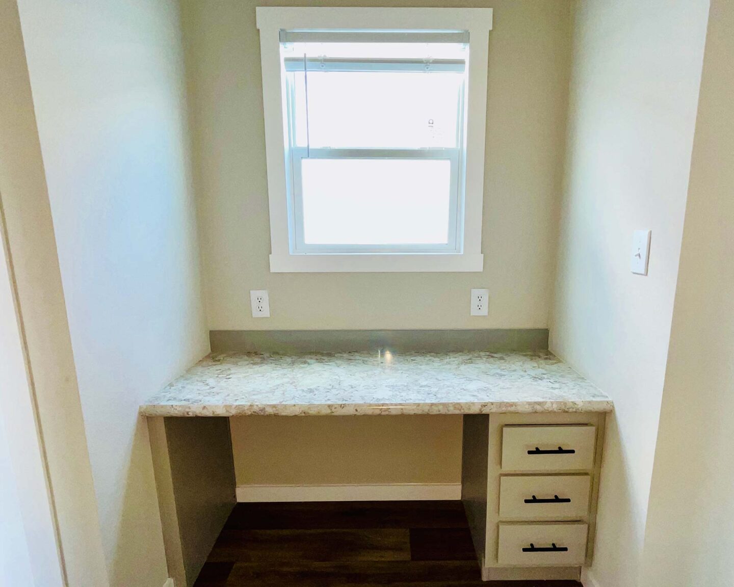 A small study nook with a marble countertop under a bright window. Three drawers are on the right, and light walls create a cozy, clean atmosphere.
