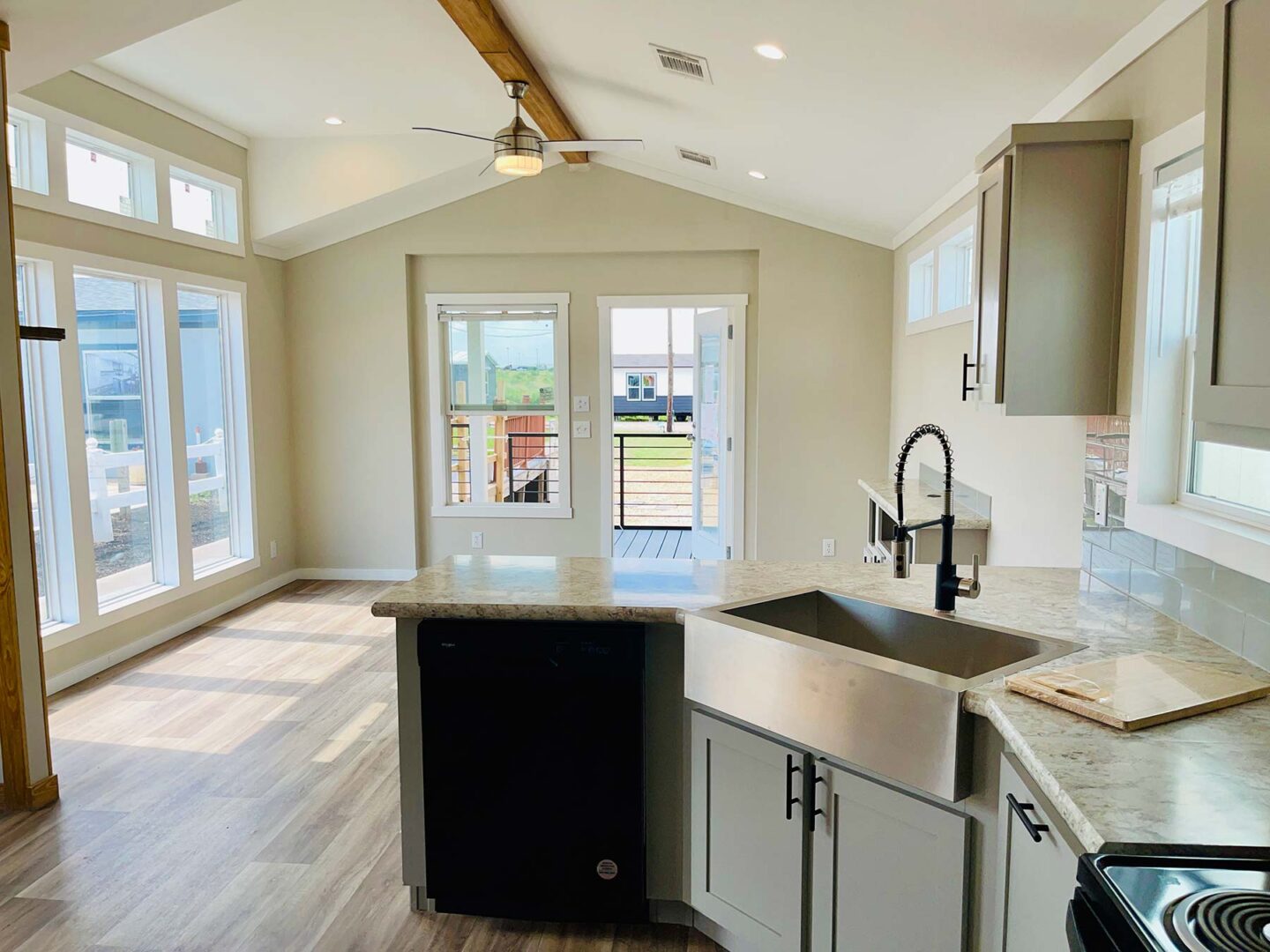 Bright, modern kitchen with marble countertops and stainless steel sink. Sunlit dining area with large windows and wood floors. Open, airy feel.