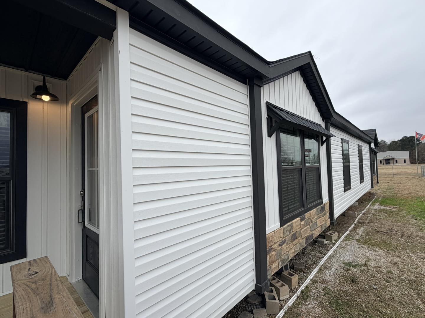 Single-story house with white vinyl siding and black trim, featuring large windows and a stone accent. Overcast sky and grassy yard create a calm setting.