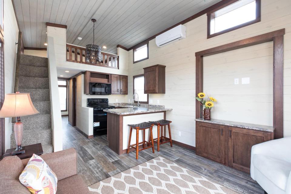Stylish tiny house interior with cozy stairs, modern kitchen featuring granite countertops, bar stools, and dark wood cabinets. Sunflowers add warmth.