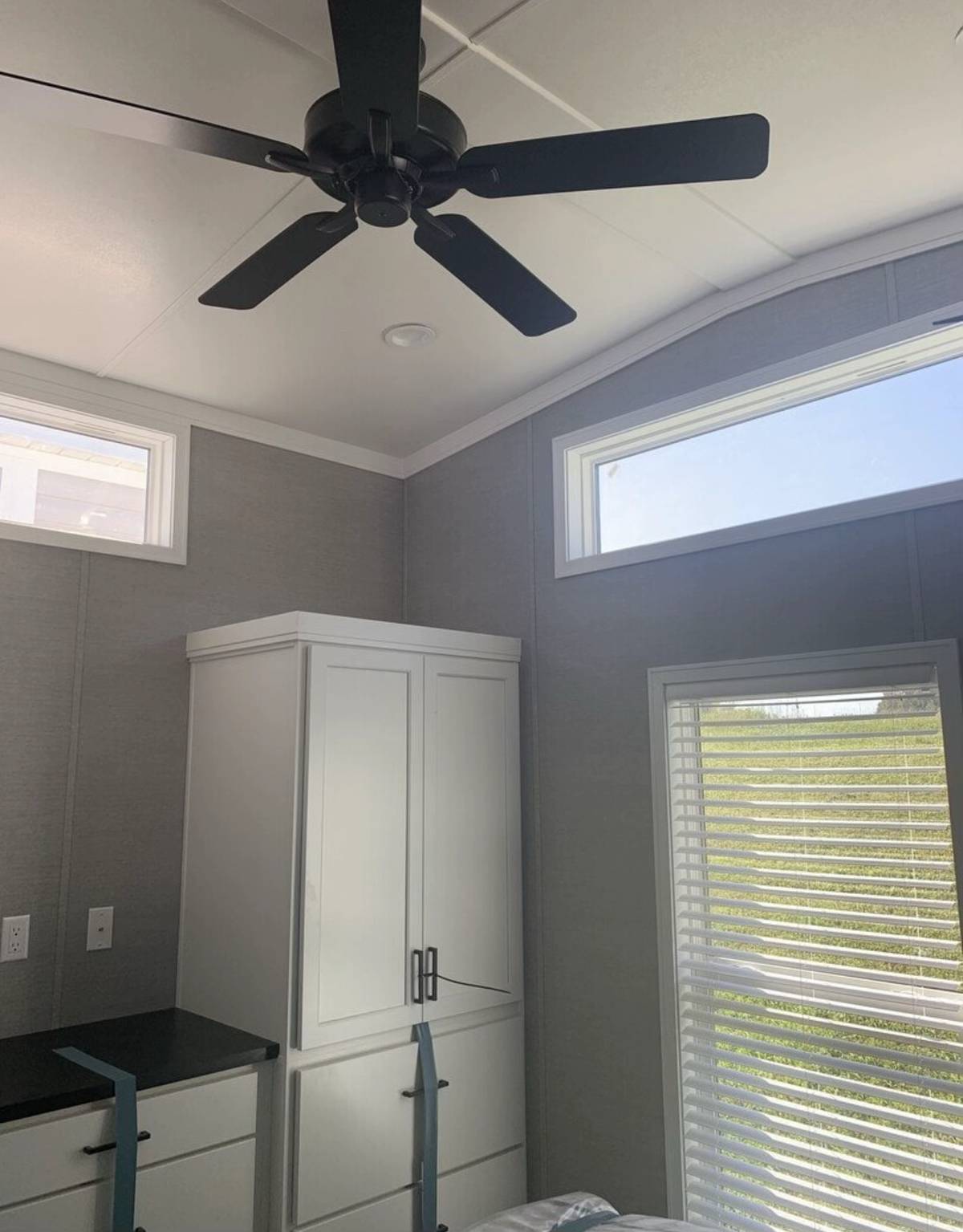 Cozy room with a ceiling fan, large window with blinds, and a white wardrobe. Sunlight streams in, creating a bright, airy atmosphere.