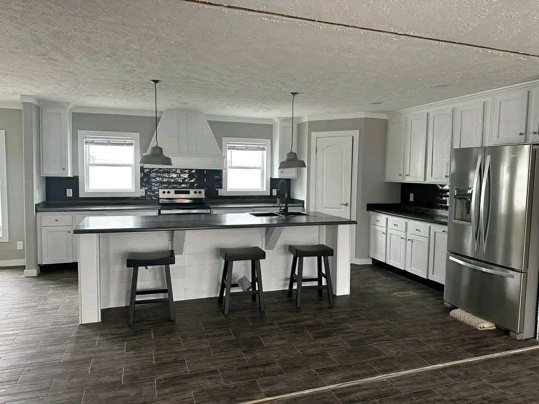 Modern kitchen with white cabinets, a black countertop, stainless steel appliances, and three barstools at the island. Pendant lights add elegance.