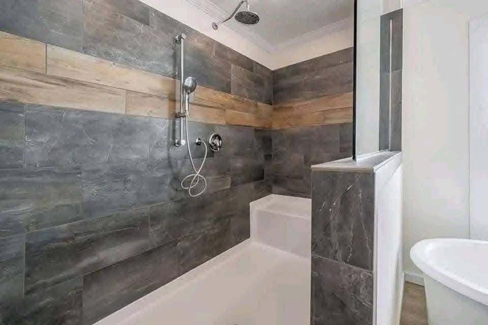 Modern bathroom with a grey and beige tiled shower. The wall features a high showerhead and handheld attachment. A bright, minimalistic design.