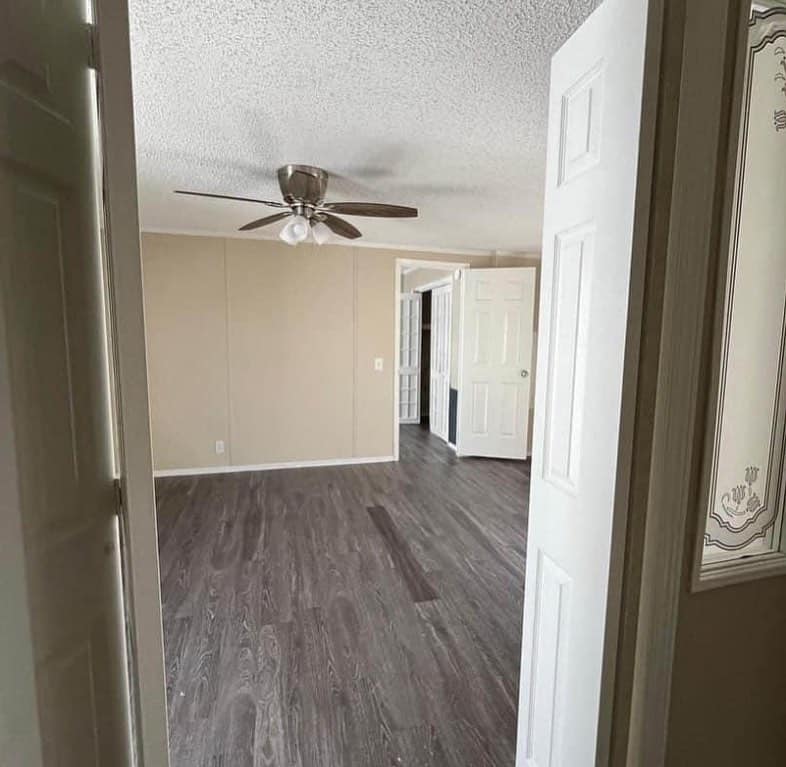 Vacant room with light brown walls, dark wood flooring, and ceiling fan. Open doors reveal a bright, inviting space, suggesting a fresh, welcoming ambiance.