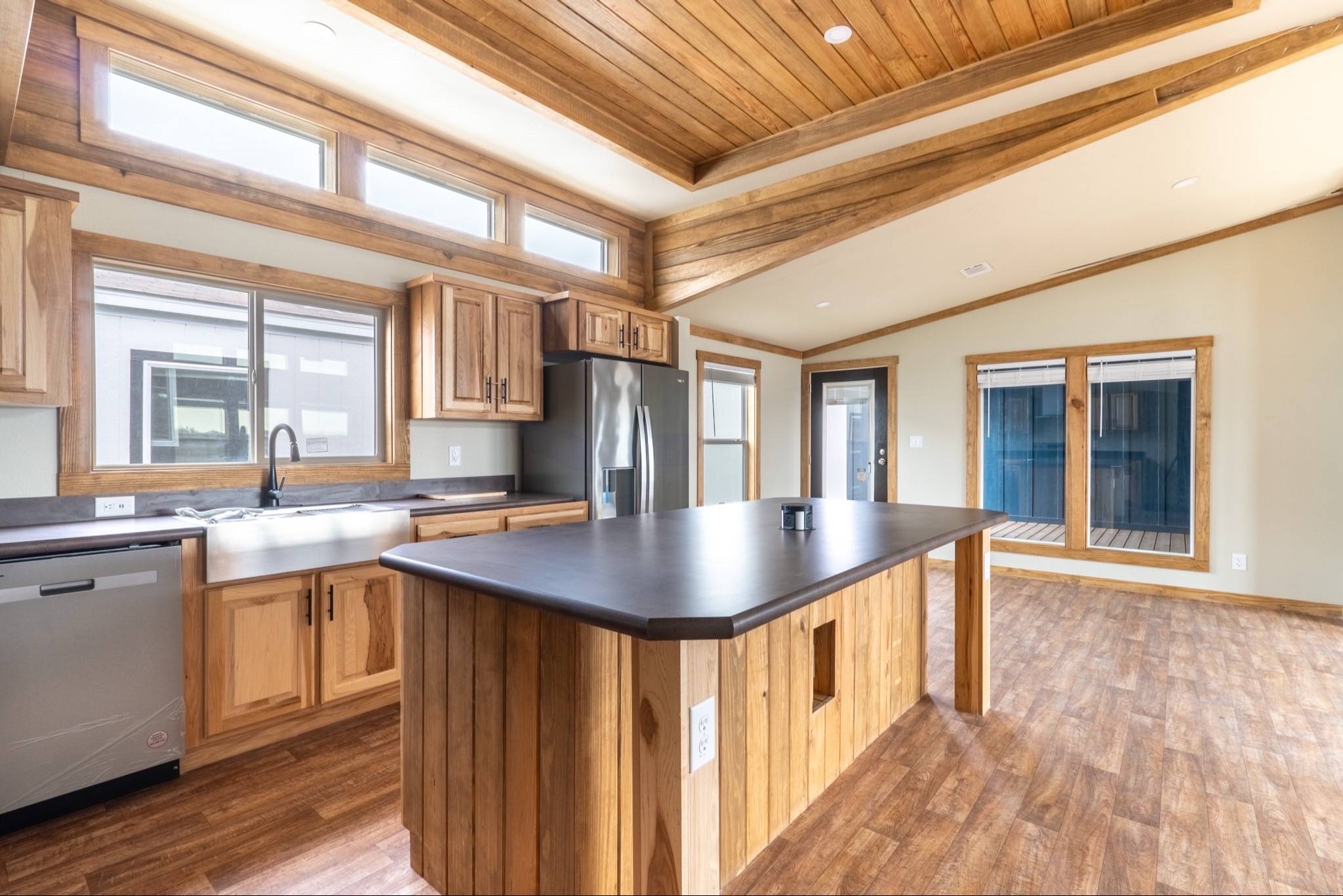 Spacious kitchen with wooden beams, light wood cabinets, stainless steel appliances, a large island with a dark countertop, and ample natural light.