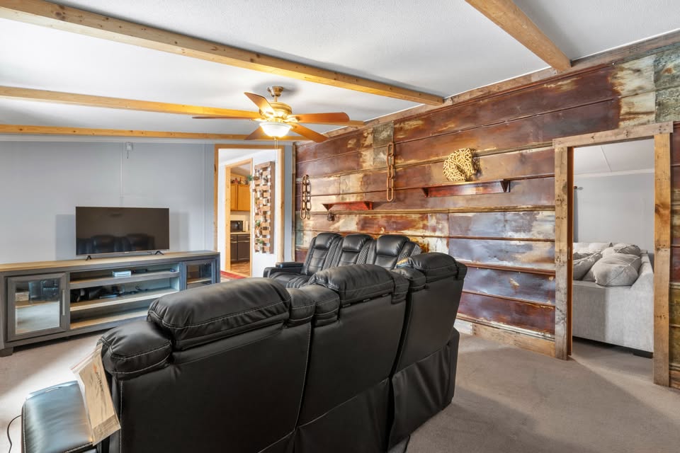 Cozy living room with black leather recliners facing a TV on a wooden stand. The rustic wood-paneled wall has decor, and a ceiling fan casts warm light.