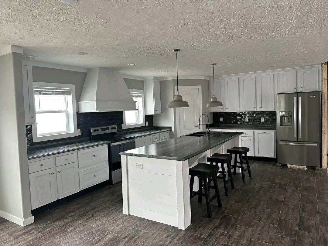Modern kitchen with a sleek design featuring white cabinets, a large island with black stools, stainless steel appliances, and pendant lighting.