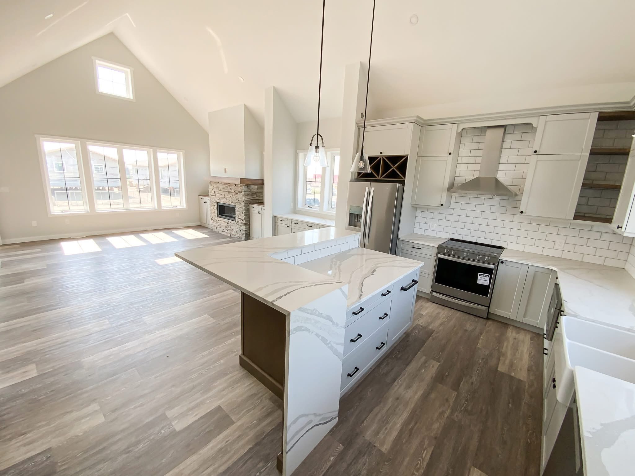Spacious modern kitchen with vaulted ceiling, large windows, and abundant natural light. Features an island, stainless steel appliances, and white cabinets.