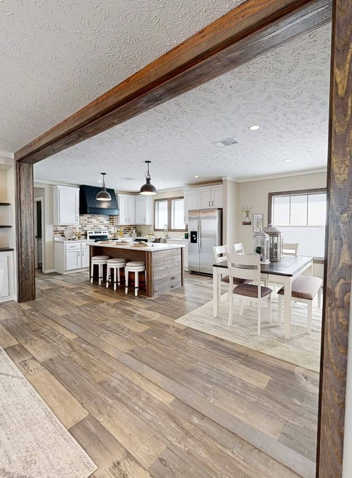 Open kitchen and dining space with wooden flooring and neutral tones. The kitchen features a large island with stools, and the dining table seats four.