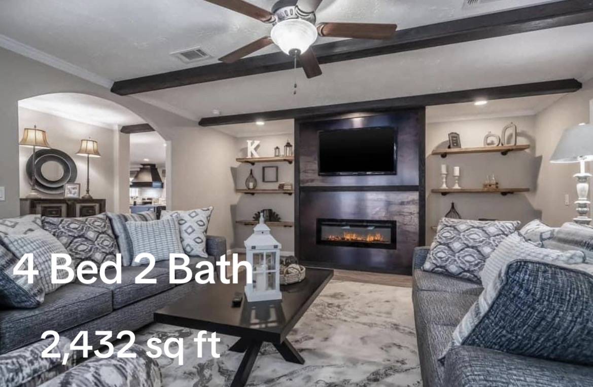 Cozy living room with two large gray sofas, a dark coffee table, wall-mounted TV, and fireplace. Text overlay: "4 Bed 2 Bath, 2,432 sq ft."