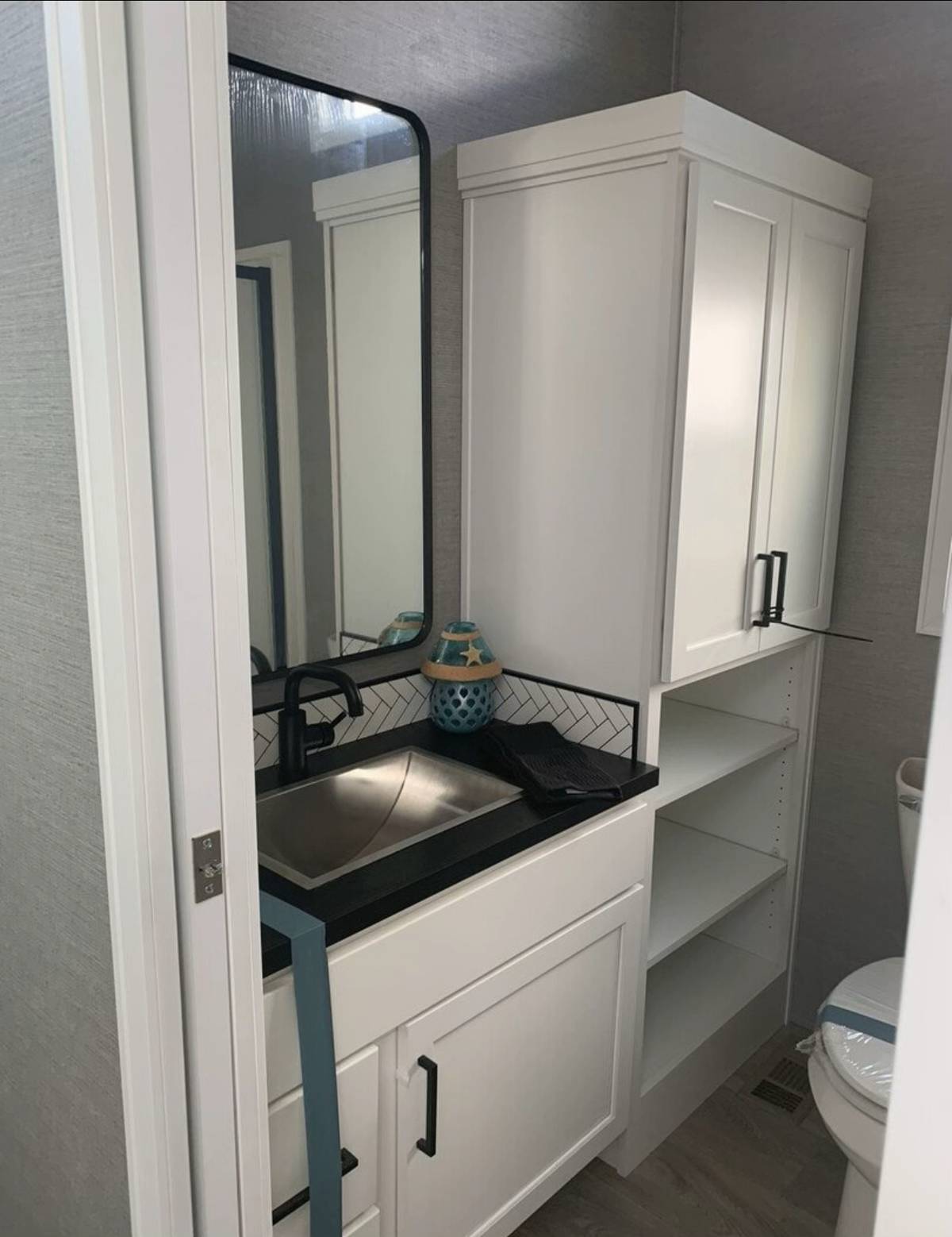 Modern bathroom with white cabinetry, black countertop, and rectangular mirror. A blue ornament sits beside a sleek faucet. Minimalist and clean feel.
