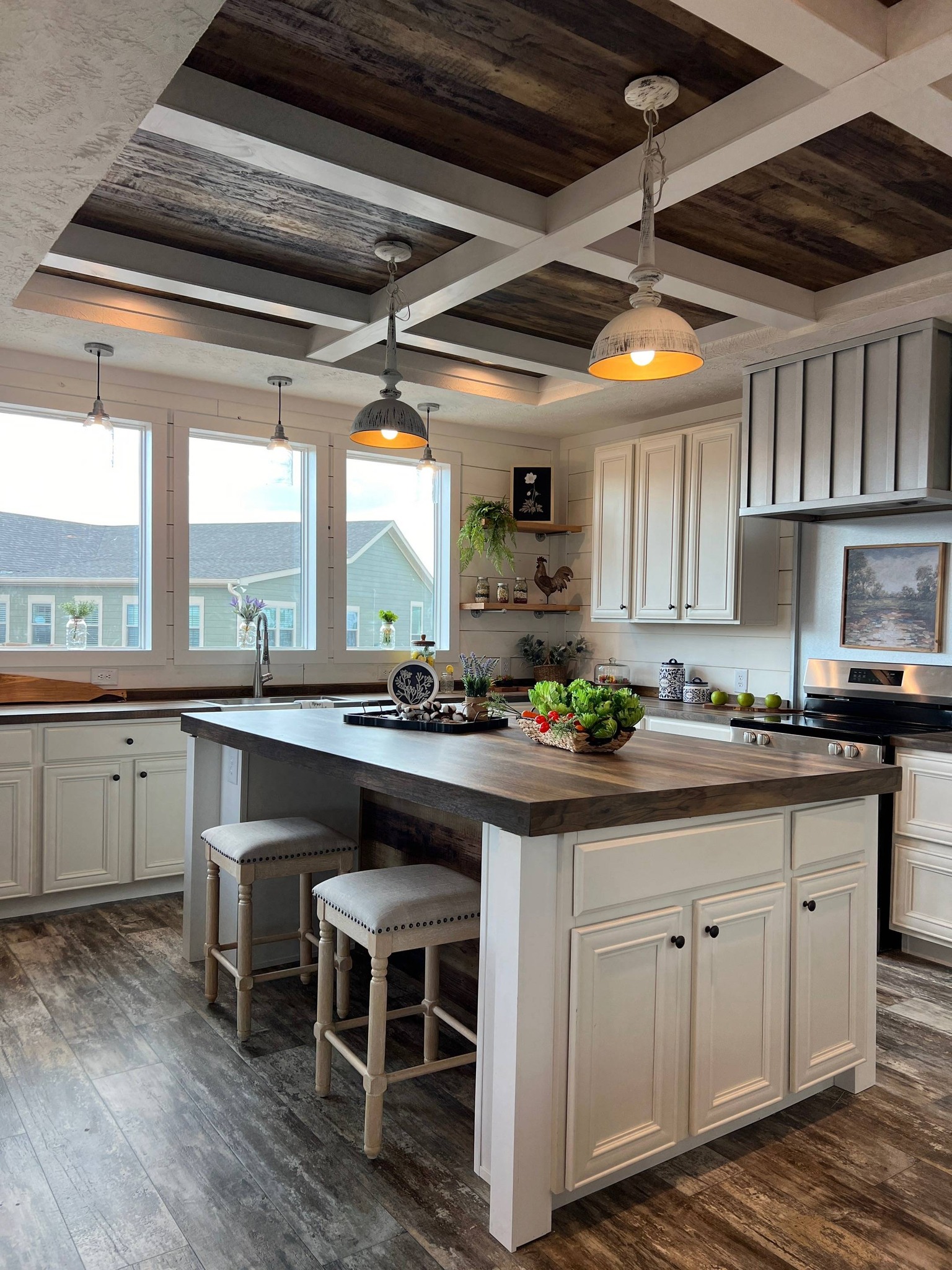 Rustic kitchen with wood-accented coffered ceiling, large island with stools, and bright windows. Neutral tones convey a cozy, inviting atmosphere.
