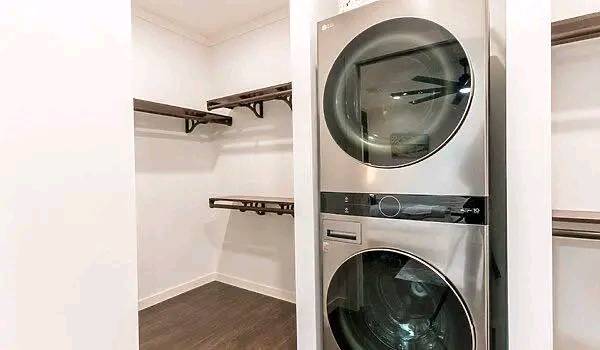 A modern laundry room with a shiny silver stacked washer and dryer. Wooden shelves line the white walls, creating a clean and organized space.