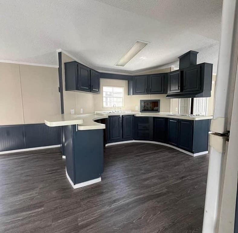 A modern kitchen with dark wood flooring and navy cabinets. A white countertop surrounds the sink, under a bright window, creating a clean, inviting space.