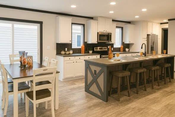 Modern kitchen and dining area; large island with stools, white cabinets, dark countertops, wooden dining table with white chairs. Bright and inviting.