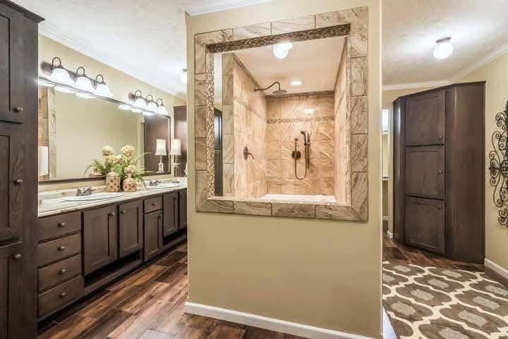 Luxurious bathroom with dual sinks, warm wood cabinets, and a central open shower tiled in beige. Elegant decor and soft lighting create a cozy ambiance.
