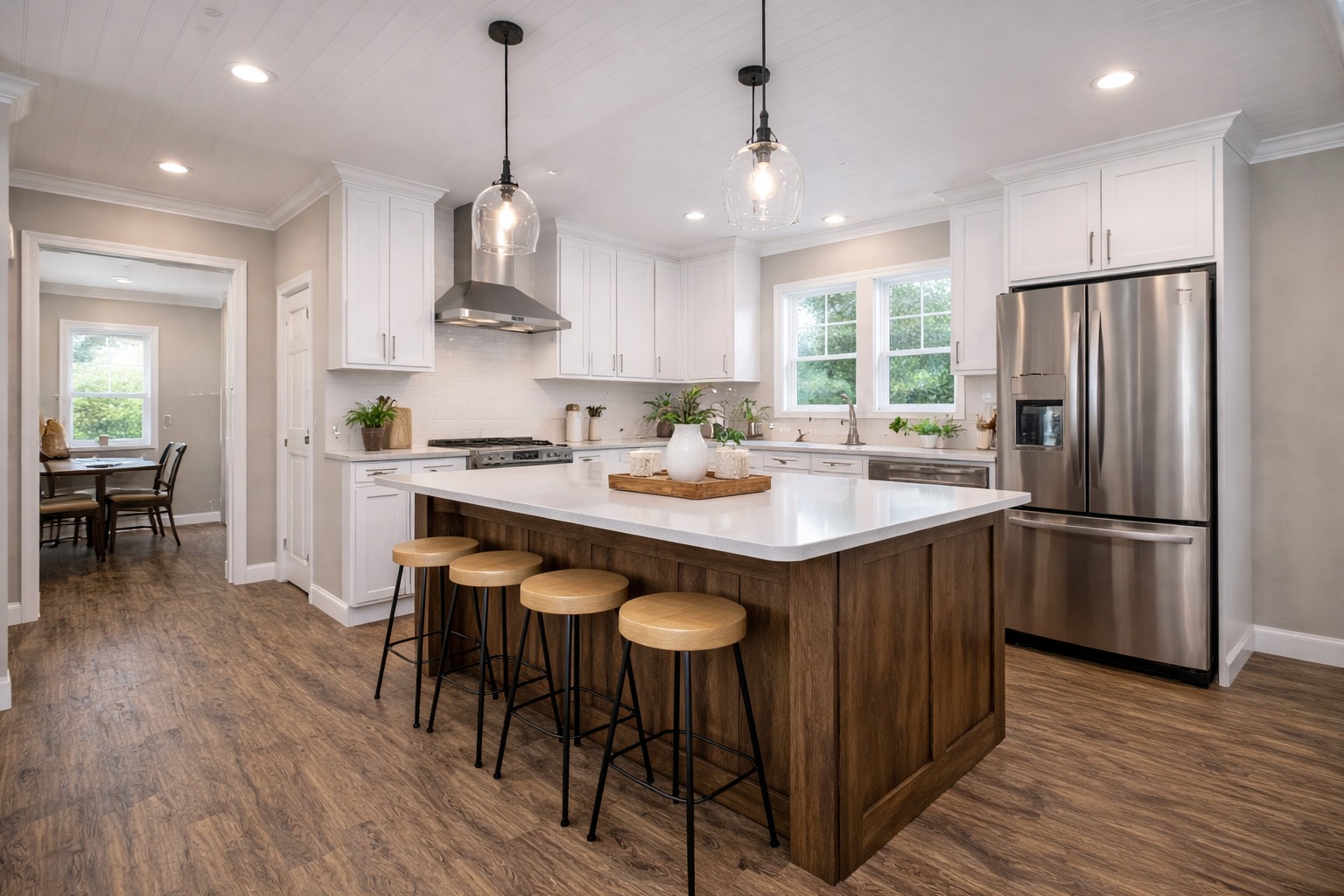 Modern kitchen with a large wooden island, white countertops, and pendant lights. Stainless steel appliances, white cabinets, and wooden stools add warmth.