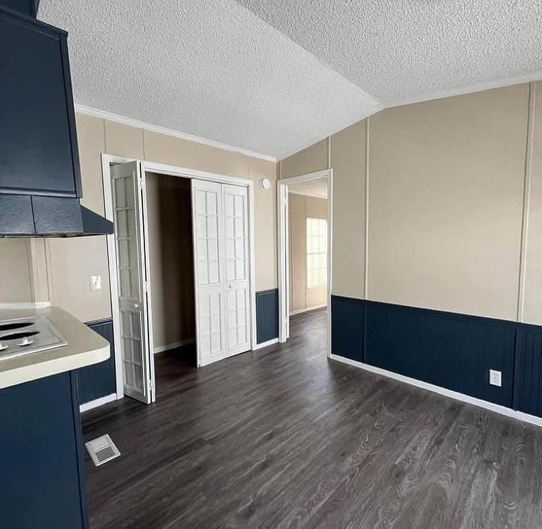 Empty room with beige walls, dark wainscoting, and sleek dark wood floors. It features white French doors leading to another room and a small countertop area.