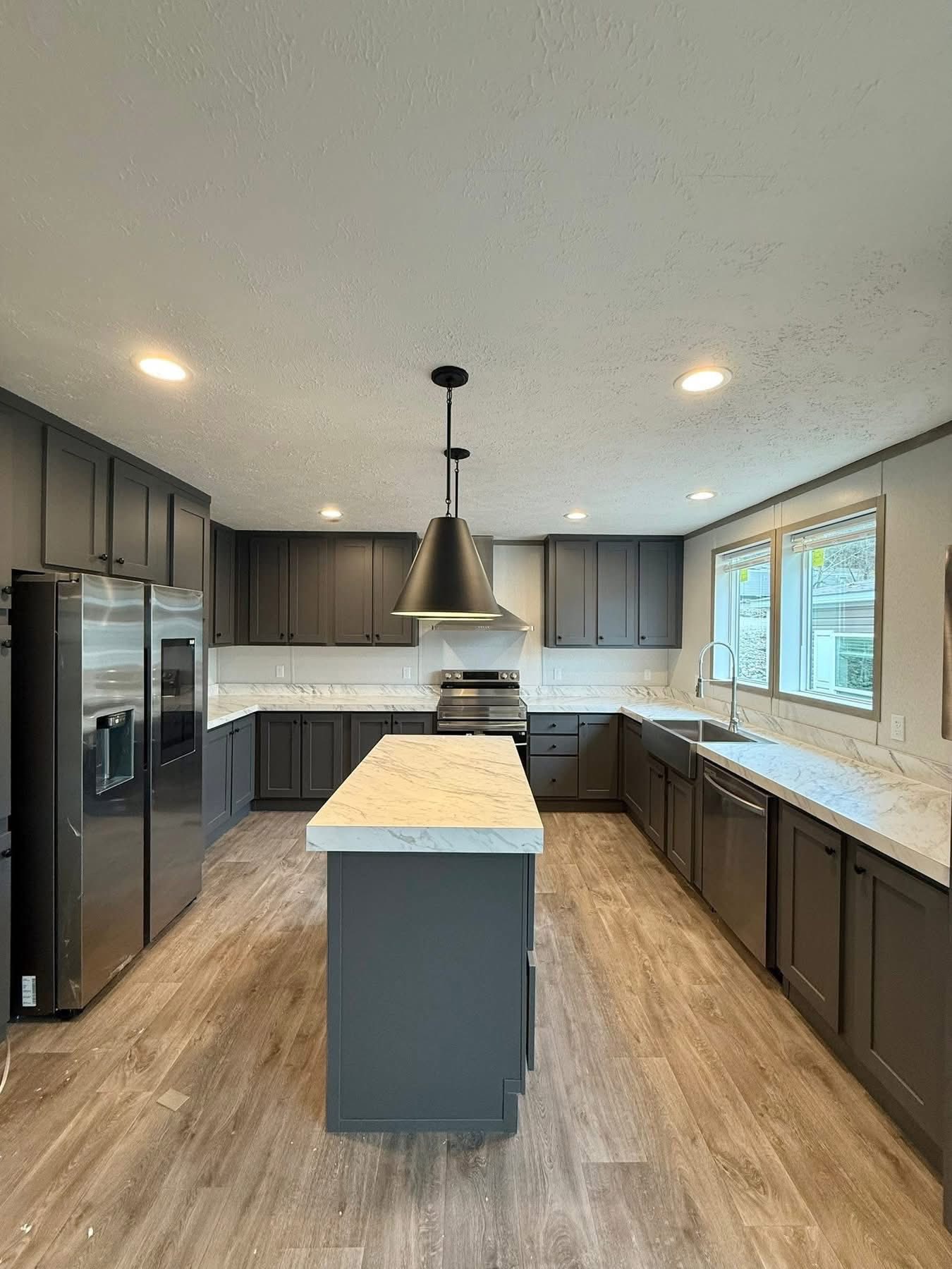 Modern kitchen with dark cabinets, marble countertops, and wood flooring. Features include stainless-steel appliances, an island, and pendant lighting.