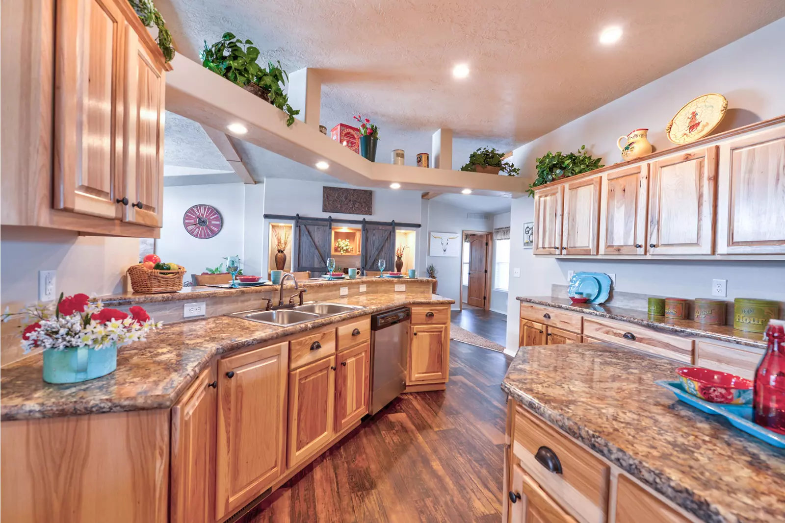 Spacious kitchen with warm wood cabinets, marble countertops, and decorative plants. Modern appliances and cozy accents create an inviting atmosphere.