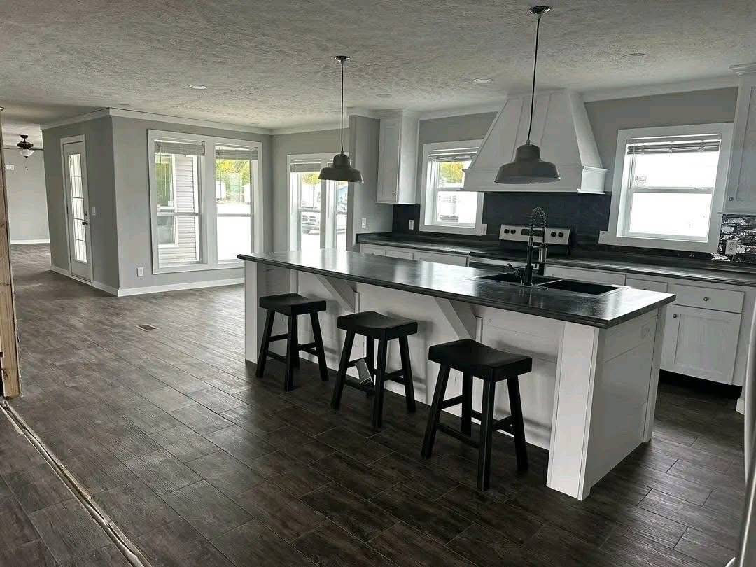 Modern kitchen with a dark wood floor, large central island with black bar stools, pendant lights, and white cabinetry. Bright, airy atmosphere.