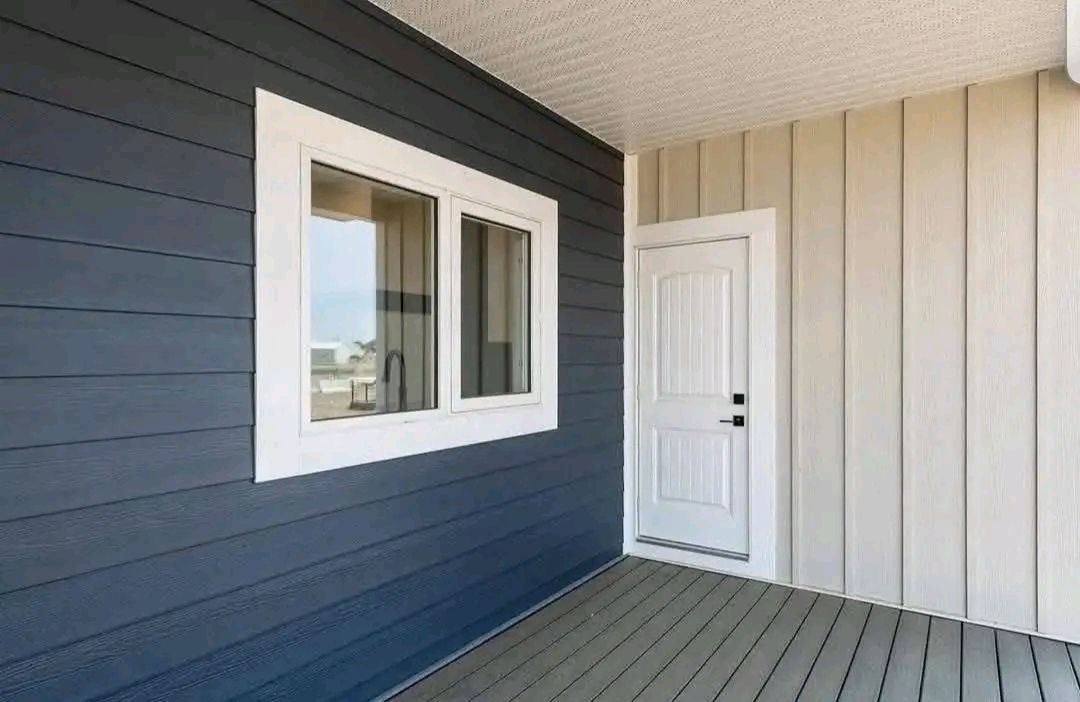 A modern porch with contrasting siding: dark blue on the left wall with a white-framed window, and beige on the right with a white door, creating a clean, serene feel.