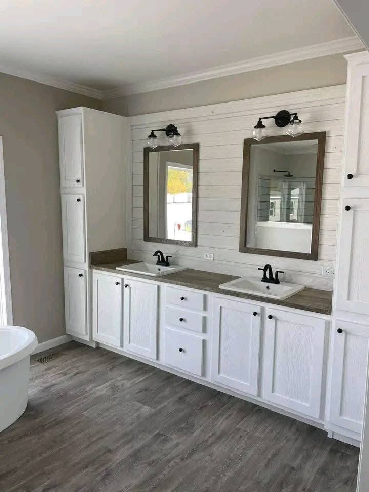 Spacious bathroom with dual white sinks, dark faucets, and wooden countertops. Two bordered mirrors and rustic lights on white shiplap wall. Modern decor.
