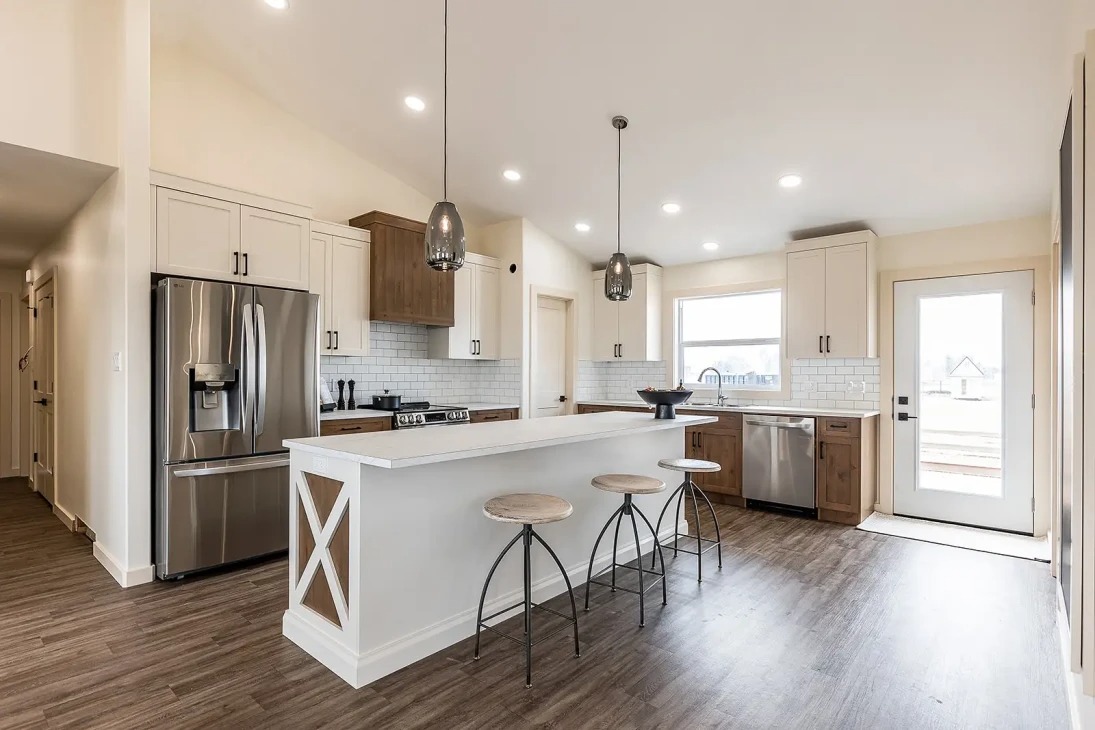 Modern kitchen with white cabinets, stainless steel appliances, and wooden accents. Features a large island with barstools and pendant lights, creating a bright, welcoming space.
