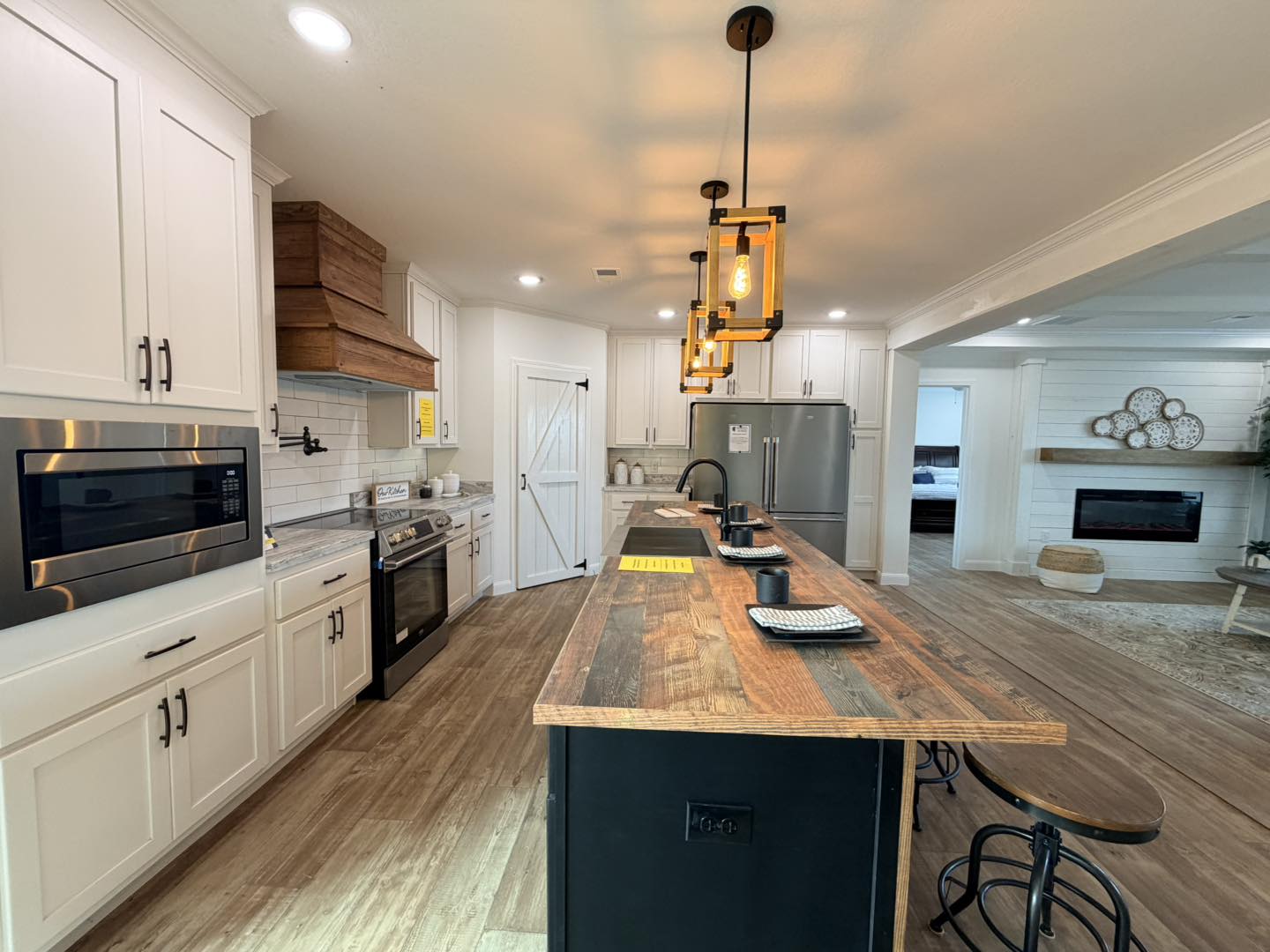 Bright, modern kitchen with wood island, hanging lights, and bar stools. White cabinets, stainless steel appliances, and an open living area evoke warmth.