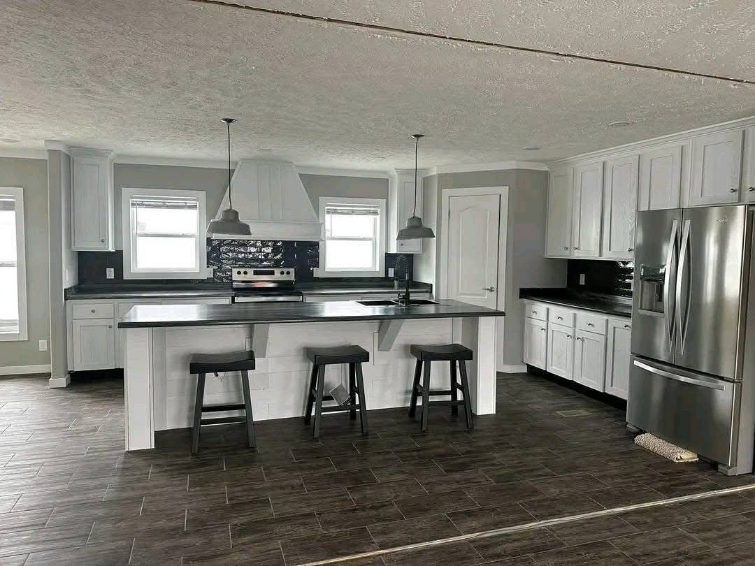 Modern kitchen with sleek design featuring gray tones. Includes stainless steel appliances, an island with three stools, and pendant lights, conveying a minimalist and clean ambiance.