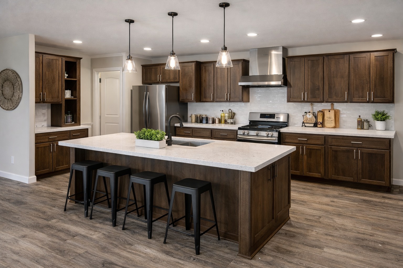 Spacious modern kitchen with dark wood cabinets, stainless steel appliances, and a large island with white countertop. Pendant lights add warmth.