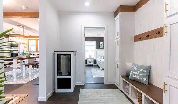 Bright hallway with white walls, a bench with a pillow that reads “We are all dreamers,” and wooden hooks. Leads to a kitchen and living area. Cozy and inviting.